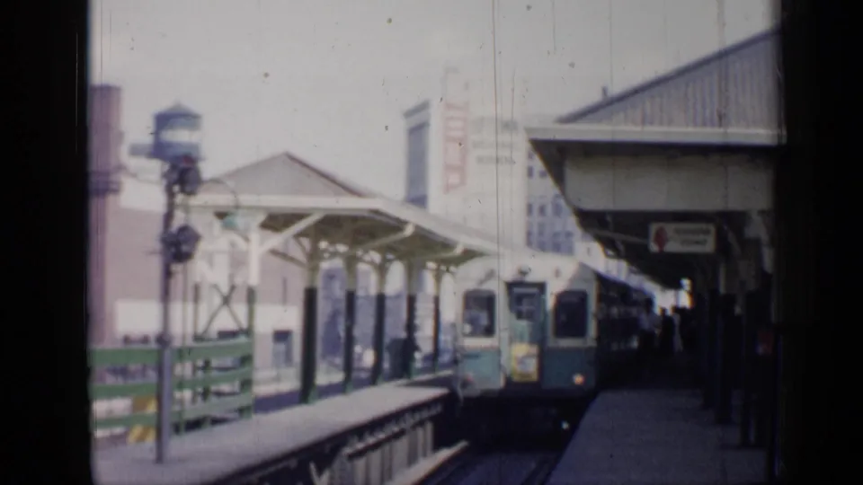 The rail car pulls toward the Chicago station platform, framed by a canopy, railing, signal post, and distant urban buildings.