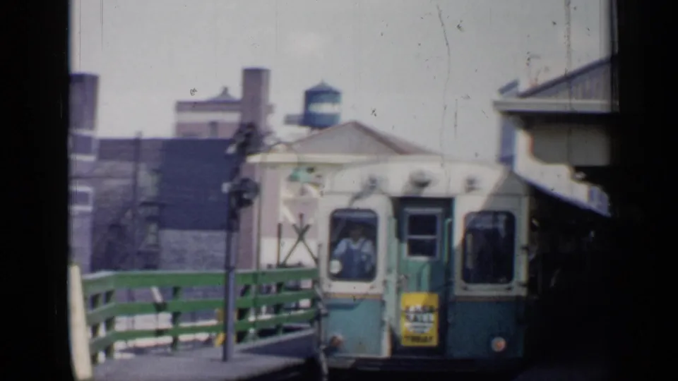 A green-and-white rail car reaches the platform in 1958 Chicago, with a person visible in the cab and station structures around it.