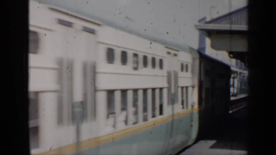 A soft 8mm frame shows the passing train at the station, with faint passengers visible through the lower windows.