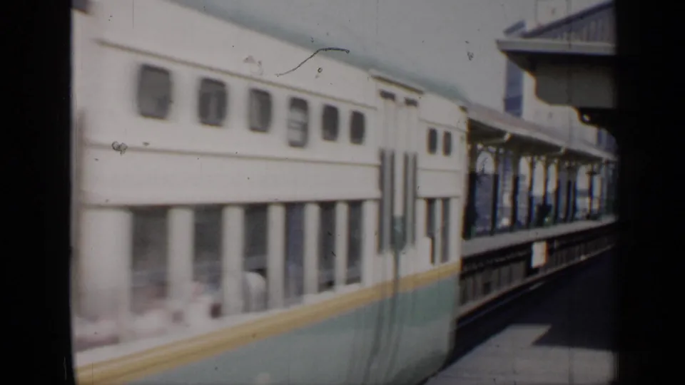 The passenger train continues past the Chicago station platform, showing window rows, teal lower paint, and platform supports.
