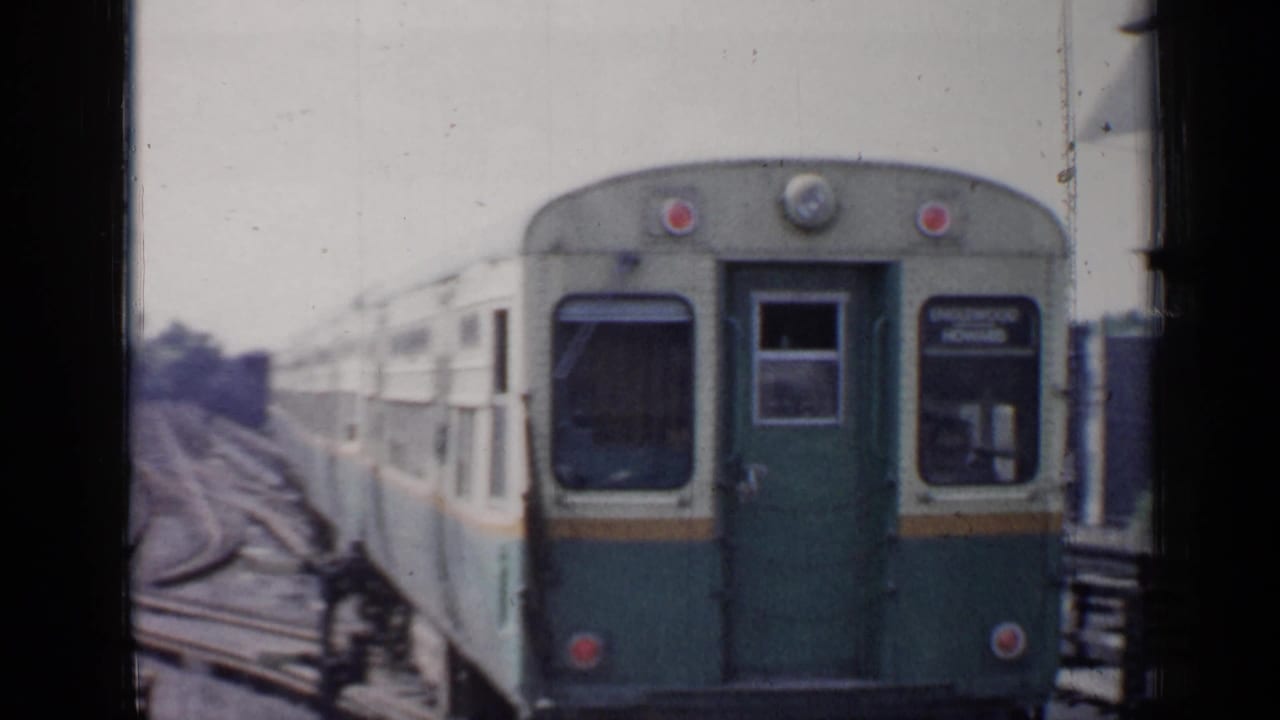 Green-and-cream rail car seen close on tracks with dark film borders.