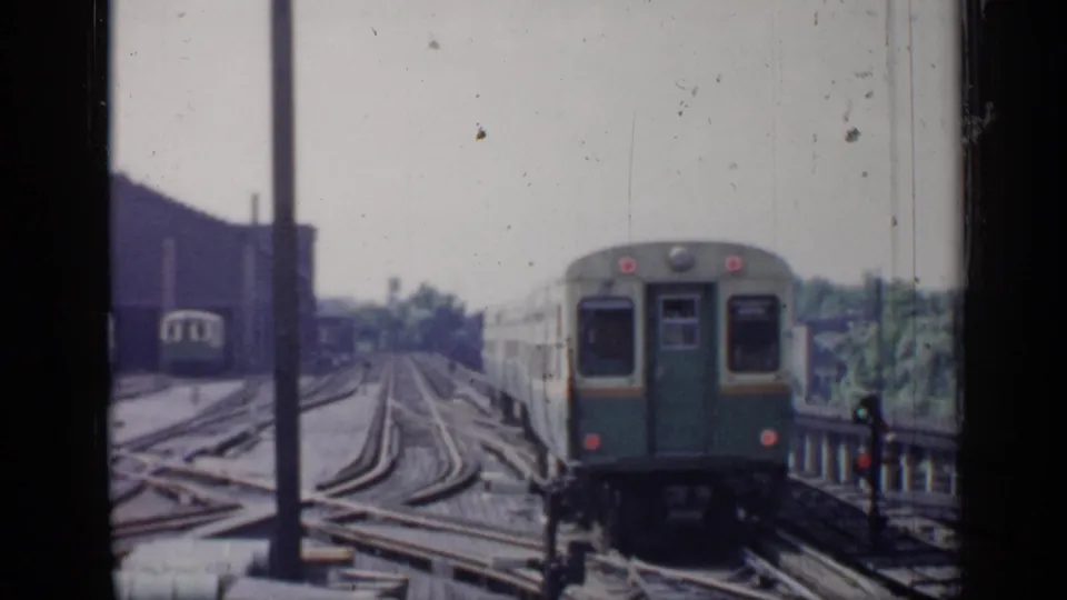 1958 Chicago 8mm view of a green-and-cream rail car moving away through a rail yard or elevated track area.