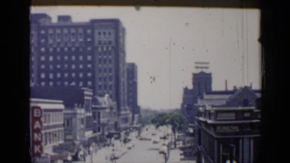 1958 Chicago home-movie frame looking down a downtown street with tall masonry buildings and visible bank signage.