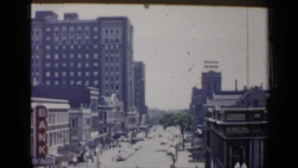 1958 Chicago 8mm frame showing a high-angle downtown street view with commercial buildings, traffic and bank signage.