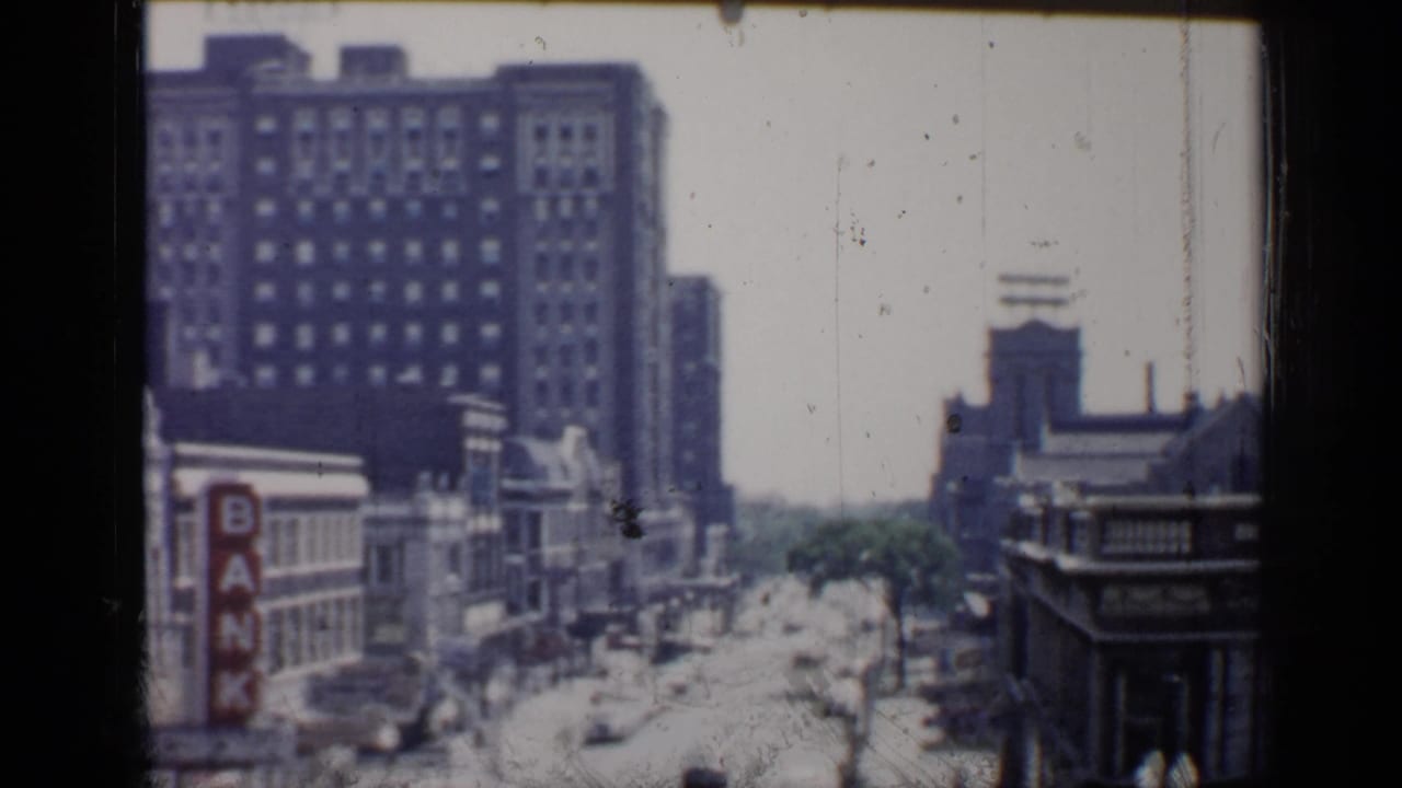 Downtown street with tall buildings, traffic, and a vertical bank sign.