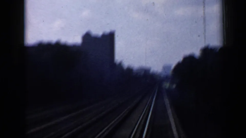 Train-window view in Chicago, with rail tracks stretching ahead between trees and dark building shapes under a cloudy sky.
