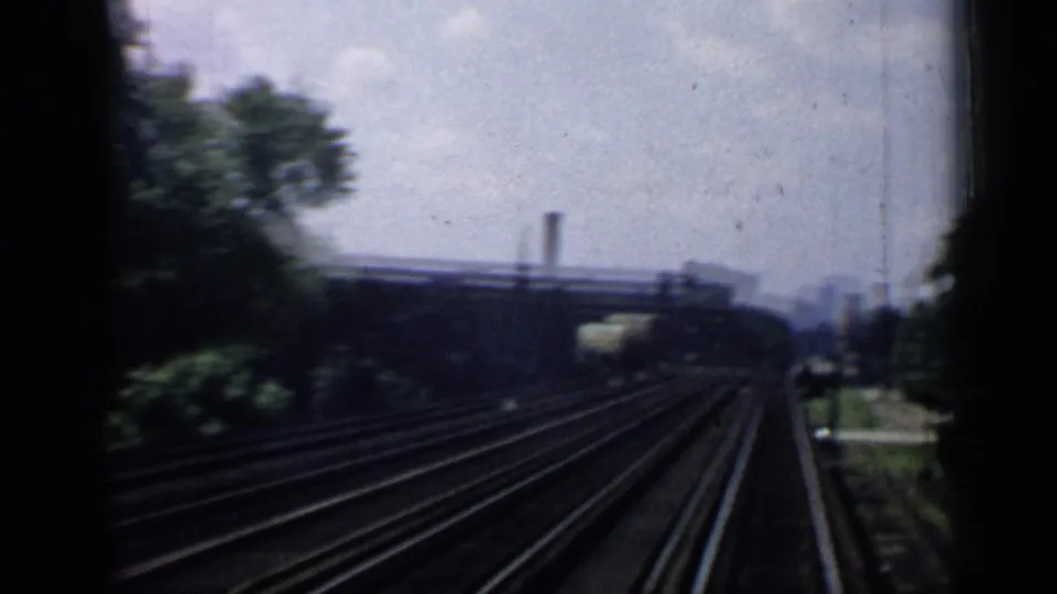 Chicago train-window view with multiple tracks, green trees, cloudy sky, and distant industrial-looking structures.