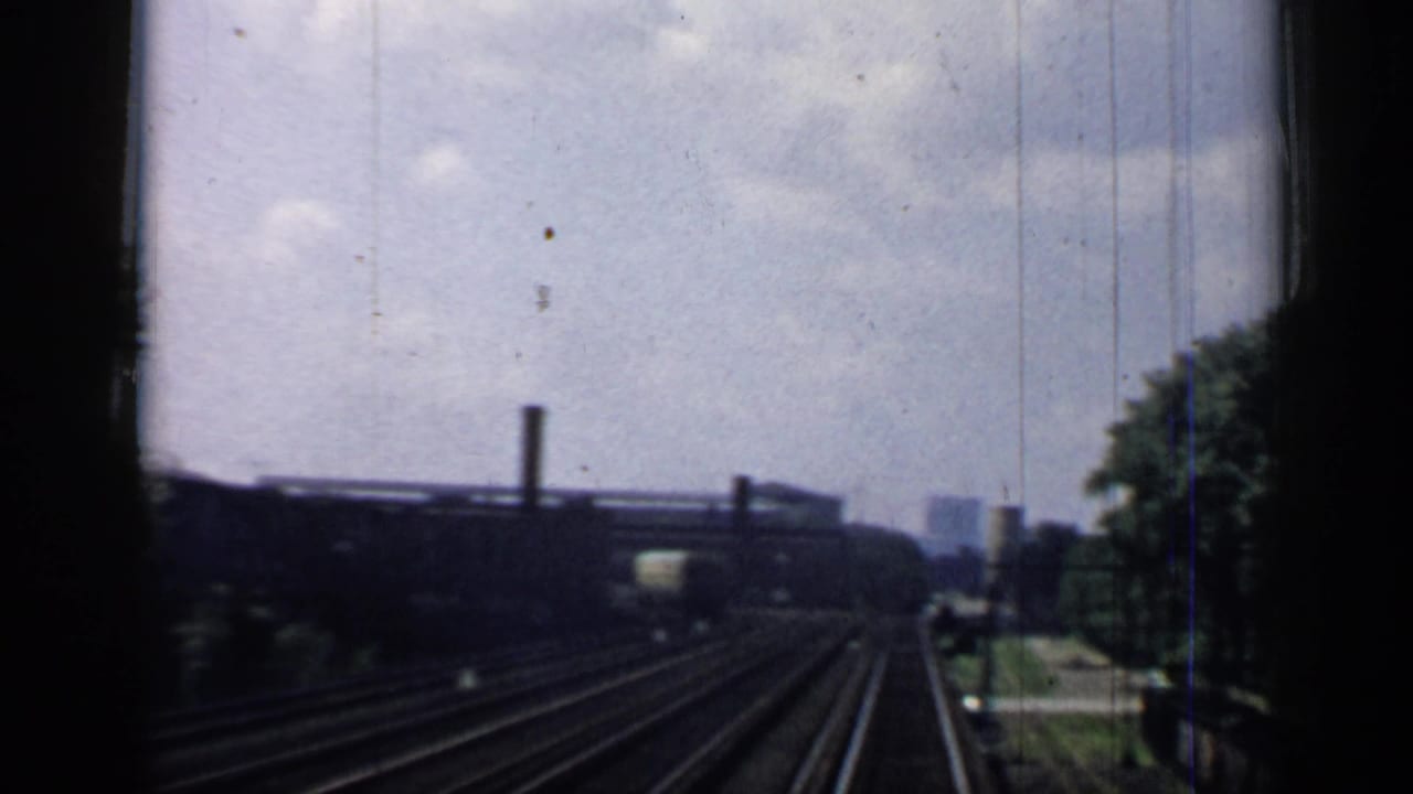 Rail tracks recede past trees and low buildings seen through a train window.