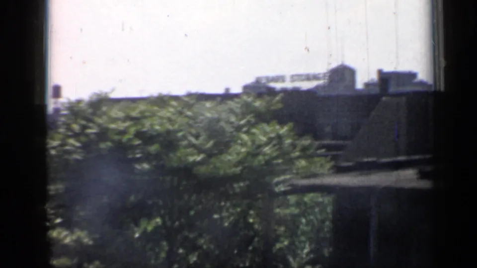 Trackside Chicago buildings and dense summer foliage blur past in a 1958 train-window home movie frame.