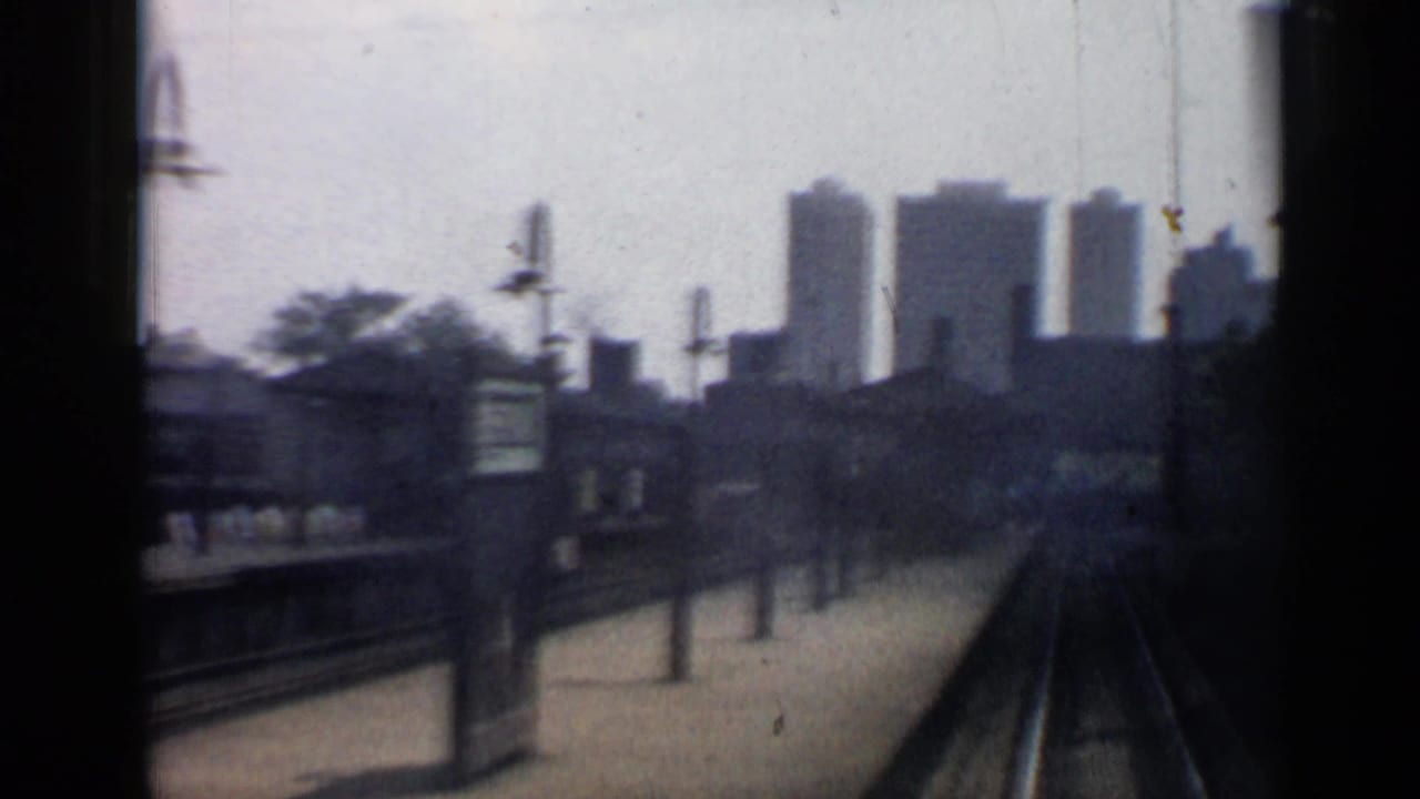 Rail tracks and station platform seen from a moving train with distant Chicago buildings.