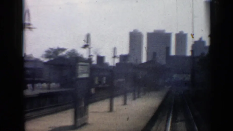 1958 Chicago train-window view of rail tracks, a platform edge, lamp posts, and distant high-rise buildings.