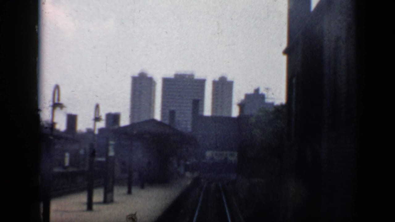 Tracks approach a station area with industrial buildings and distant towers.