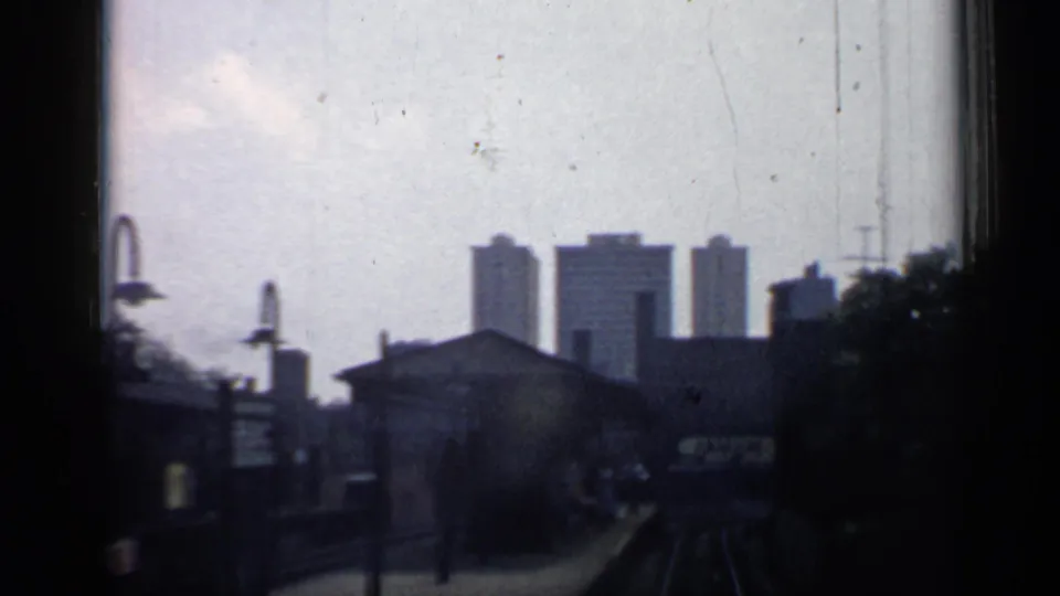 Chicago rail corridor in 1958, showing a platform, tracks, lamps, low station-side buildings, and distant high-rises.