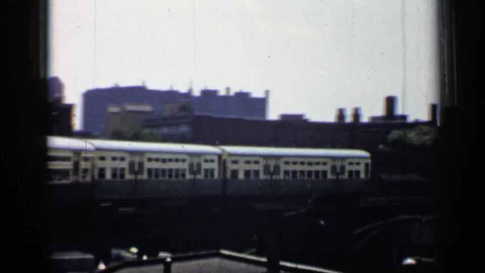 1958 Chicago train-view frame showing light-colored railcars, industrial rooflines, and distant city buildings on 8mm film.