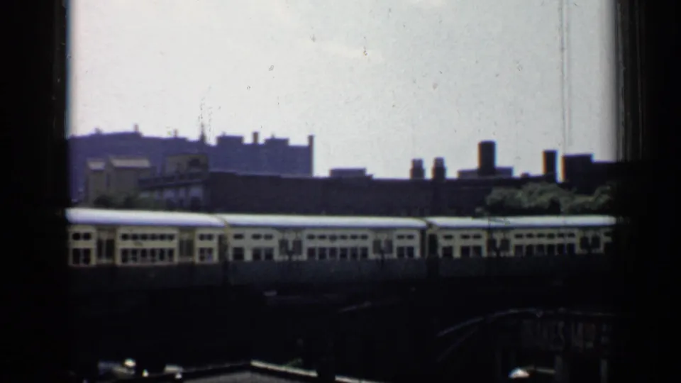 1958 Chicago rail scene with passing railcars, industrial buildings, rooftop chimneys, and soft distant skyline forms.