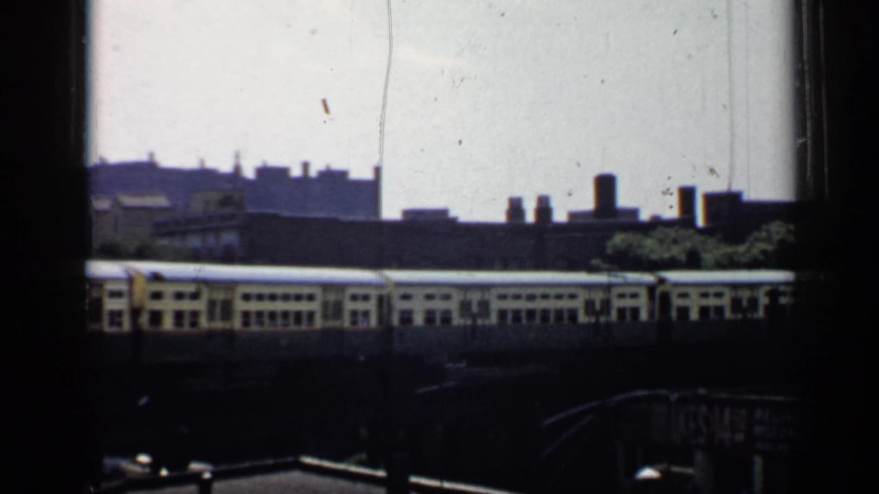 Elevated train passing behind dark foreground framing with city rooftops in the background.