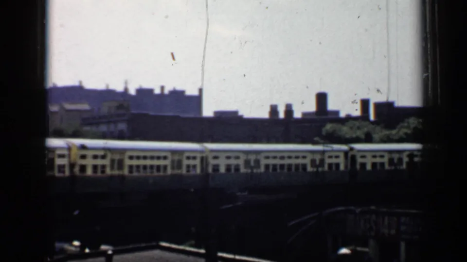 1958 Chicago home-movie frame showing an elevated train moving past rooftops, seen through dark window or structural framing.