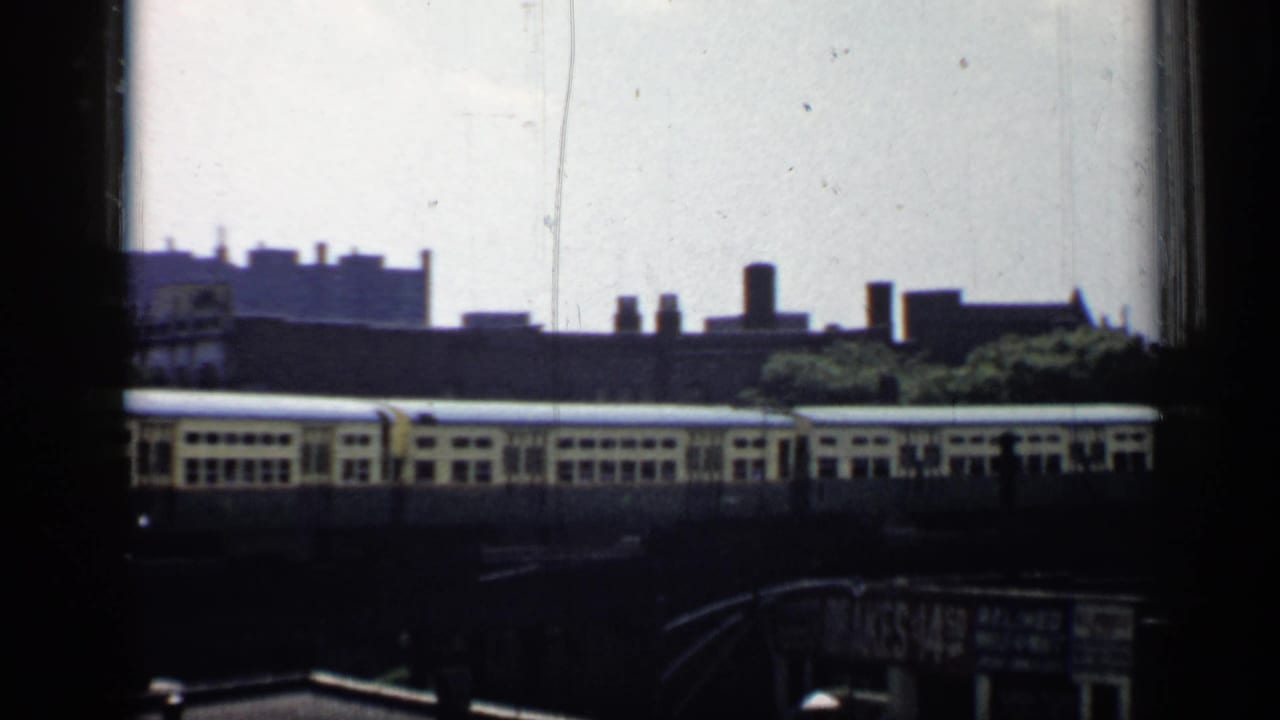 Elevated train crossing the frame with rooftops and a partially visible sign below.