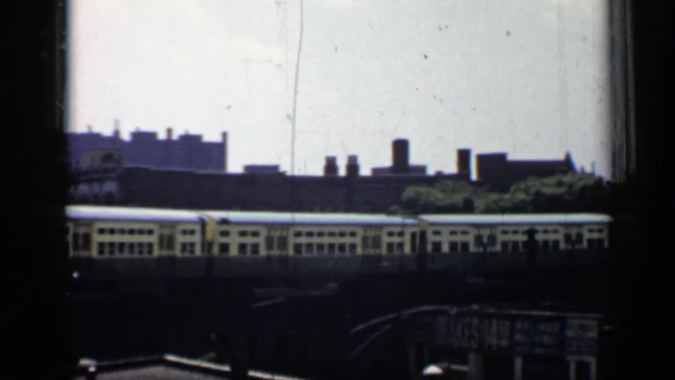 1958 Chicago frame of a train along elevated tracks, with dark foreground framing, rooftops, trees, and a partially visible sign below.