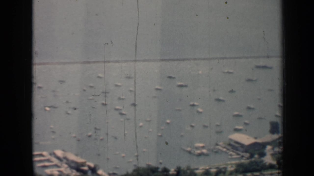 Harbor with scattered boats, a pier area at lower right, shoreline trees, and dark window framing.