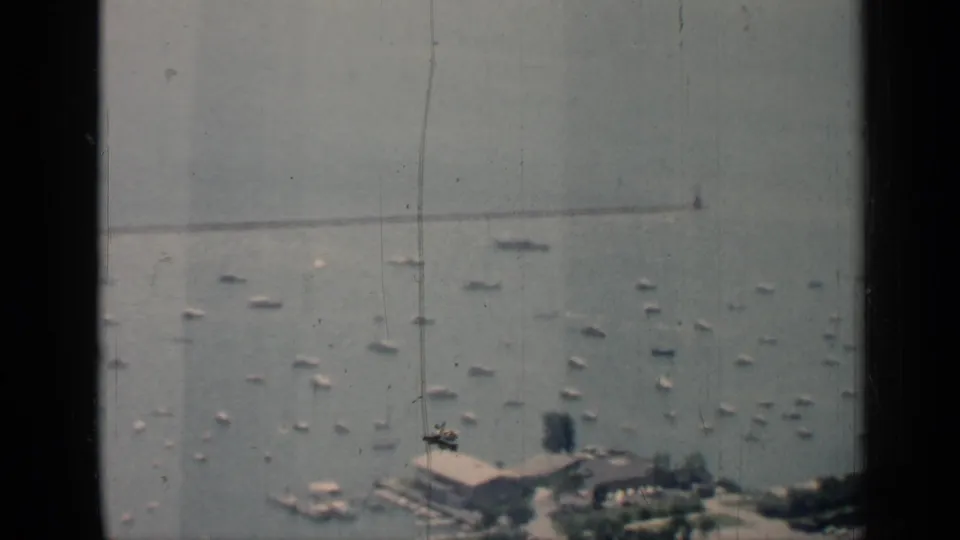 1958 Chicago waterfront view from behind window edges, with scattered boats, a shoreline pier area, trees, and a distant breakwater-like line.