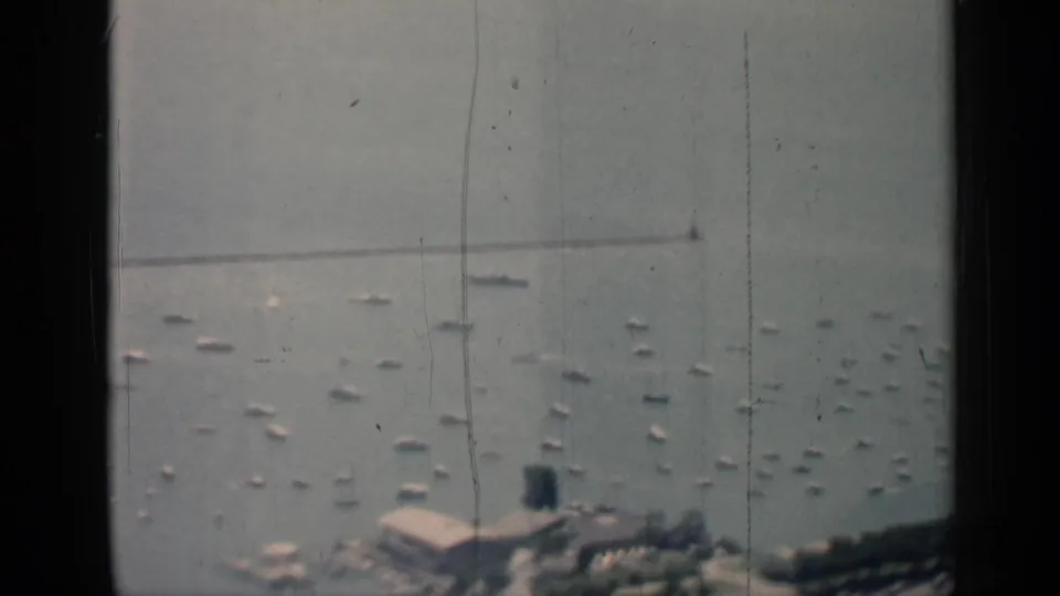 1958 Chicago harbor view through dark window edges, showing many small white boats anchored in calm water near shoreline buildings.