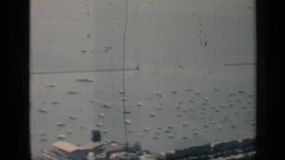 1958 Chicago waterfront frame with anchored white boats, shoreline greenery, low buildings, and a dark vertical window frame crossing the view.