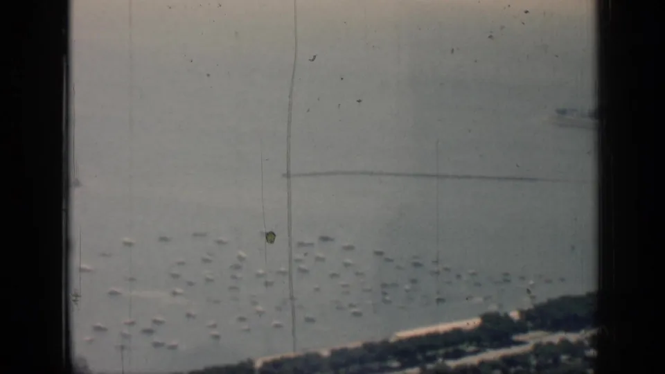 1958 Chicago waterfront seen from above, with clustered small boats on the water and shoreline structures partly obscured by 8mm frame edges.