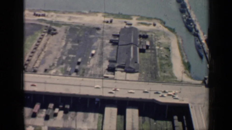 1958 Chicago shoreline from above, with cars on a highway, a waterfront lot, an industrial building, a narrow channel, and docked vessels.
