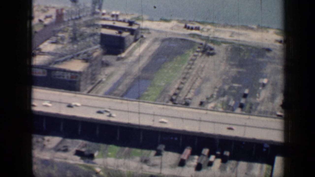 Elevated roadway crossing an industrial riverfront area with cars moving across the bridge.