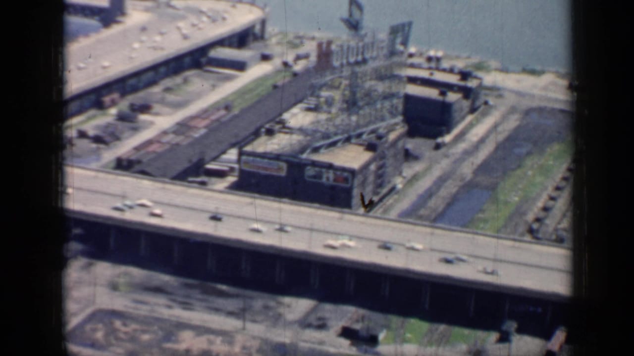 Curving elevated bridge and nearby industrial buildings beside a river with light car traffic.