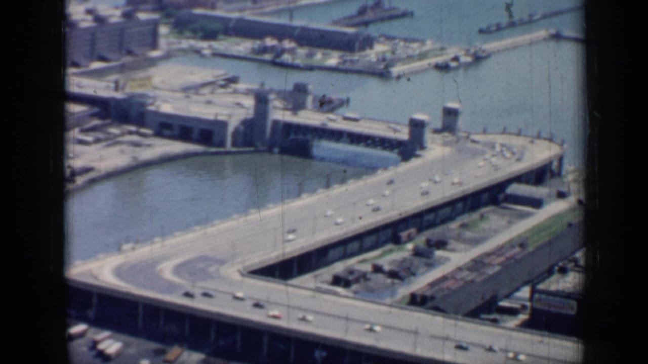 Aerial view of elevated roadway, bridge, canal, and industrial waterfront buildings.