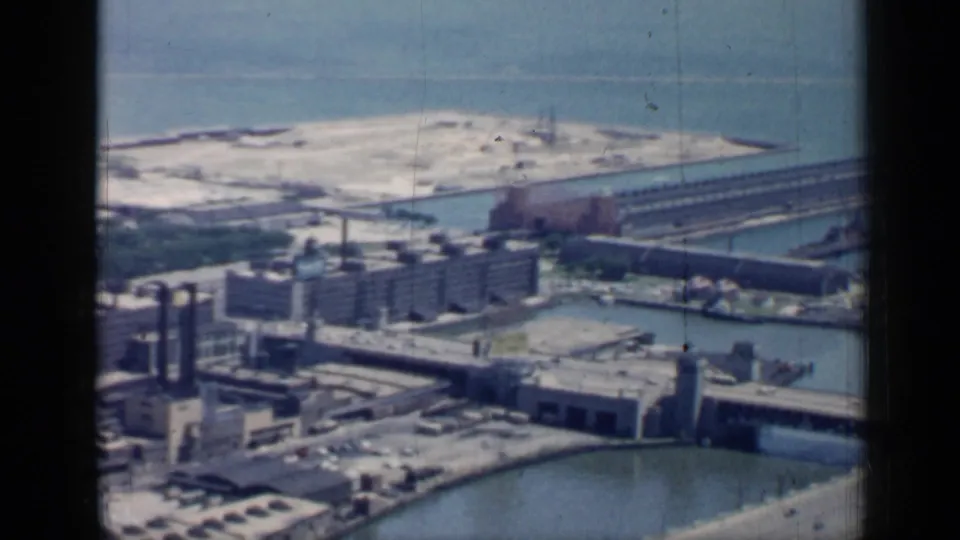 1958 aerial view across Chicago industrial waterfront facilities, water channels, bridge structures, roadways, and a long pier near open water.