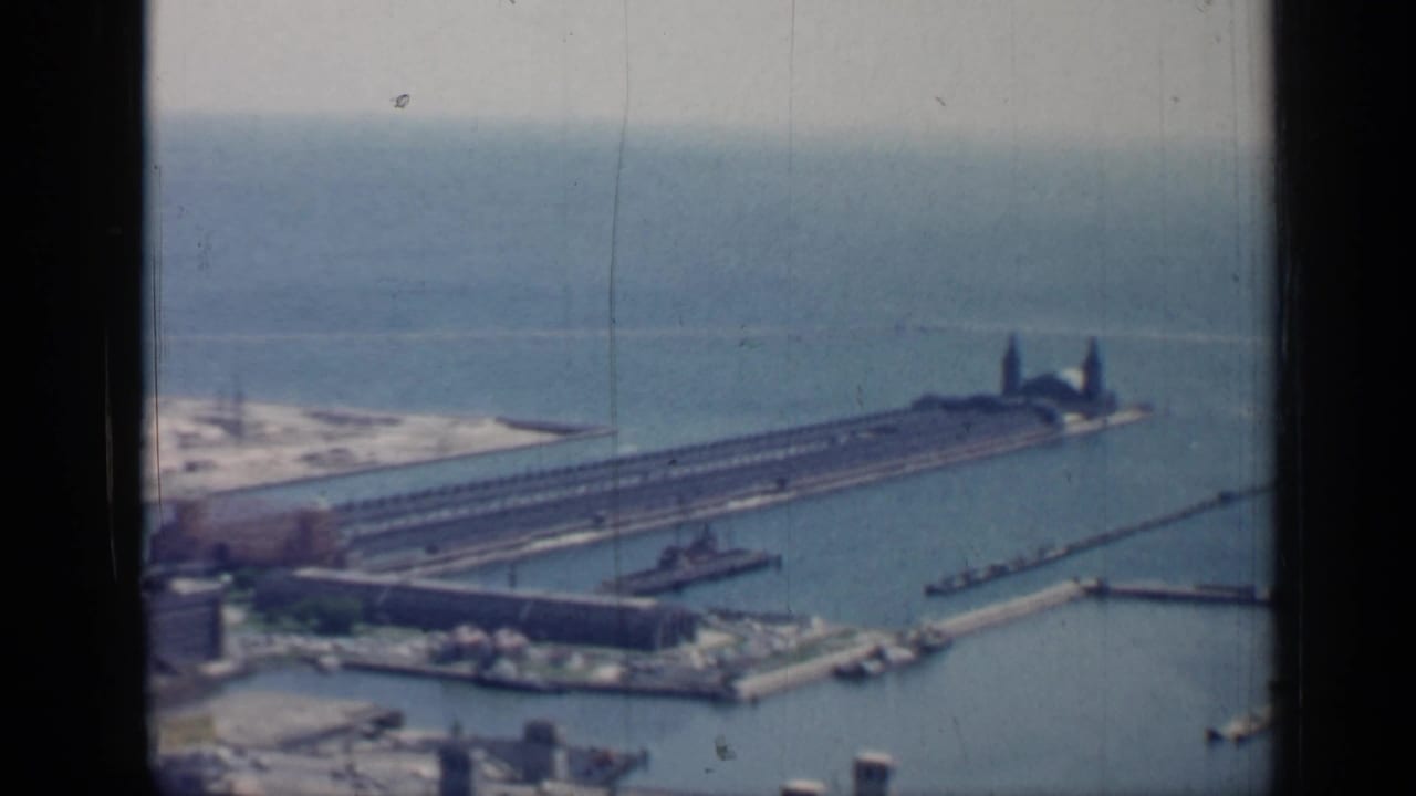Aerial harbor view with long pier, lake water, boats, industrial buildings, and dark window framing.
