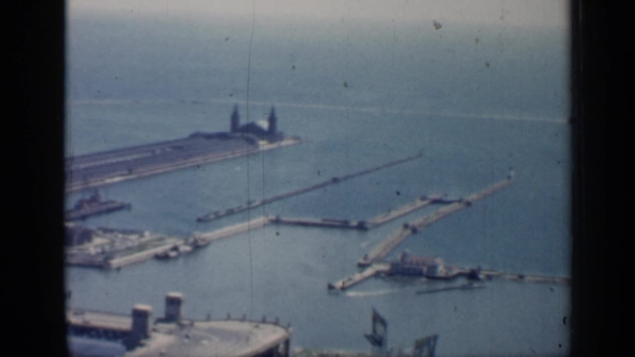 High-angle harbor view with piers, water, and a lighthouse-like structure.