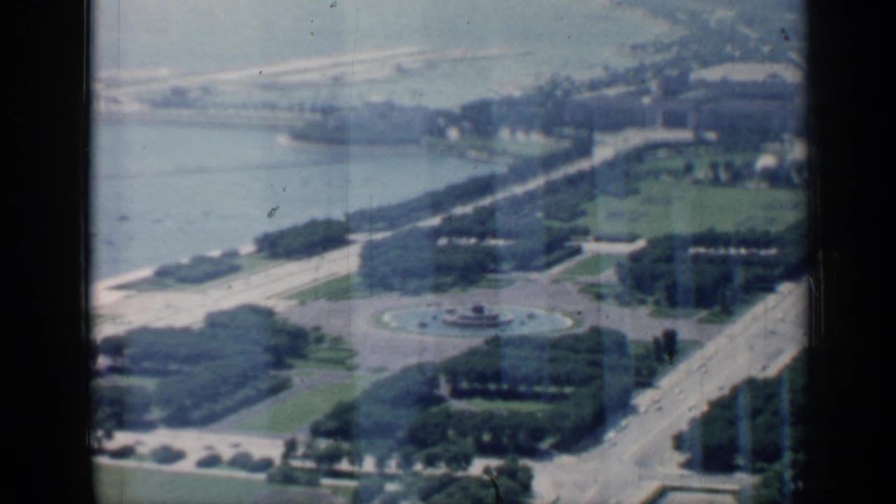 Aerial view of shoreline, formal lawns, tree rows, roads, and a round fountain.