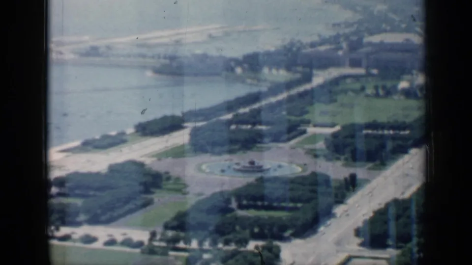 Aerial 1958 Chicago lakefront scene with a round fountain, green park blocks, shoreline, and broad roads below.