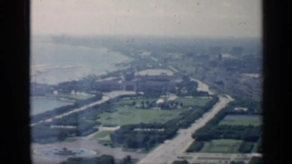 1958 airplane-window view over Chicago's lakefront, with parkland, roads, buildings, and a hazy shoreline receding into distance.