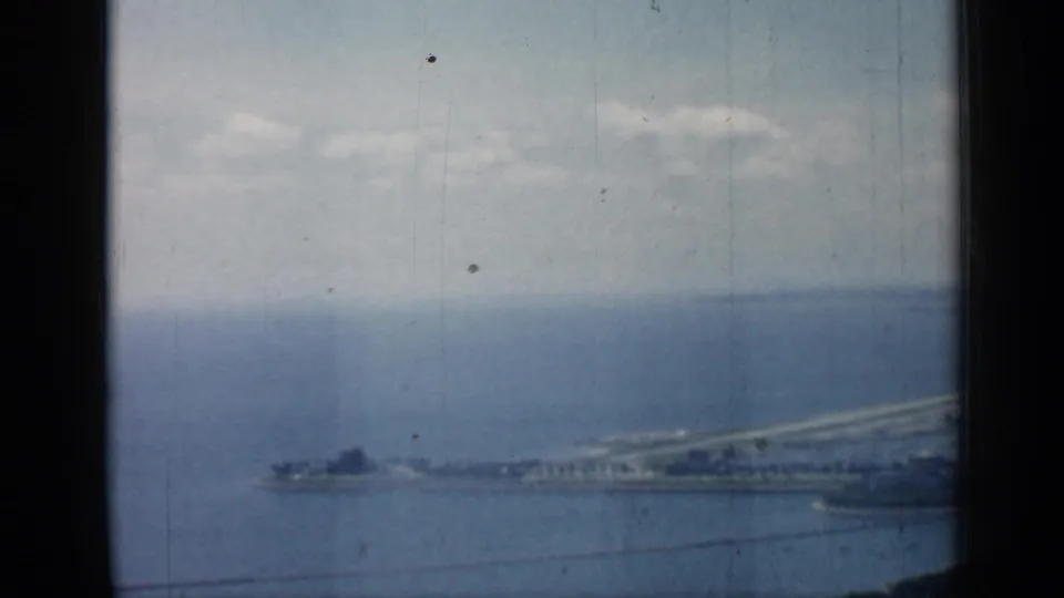 1958 Chicago aerial frame showing hazy lake water, shoreline infrastructure, a pier or breakwater, and dark aircraft-window framing.