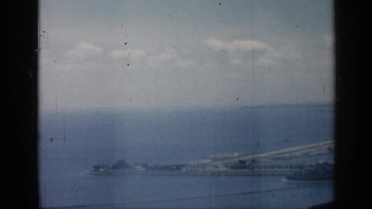 Distant shoreline and pier across blue water under cloudy sky, framed by dark film edges.
