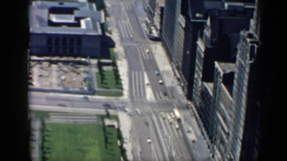 High-angle 1958 Chicago view over downtown streets with green space, moving cars, crosswalks, and dense building facades.