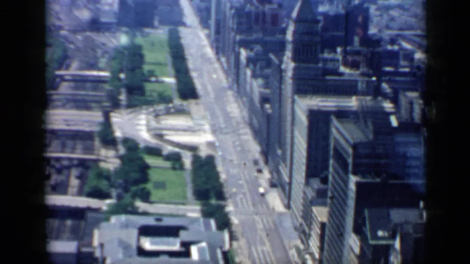1958 Chicago aerial frame with visible 8mm softness, showing downtown streets, green space, towers, traffic, and a flat-roofed building below.