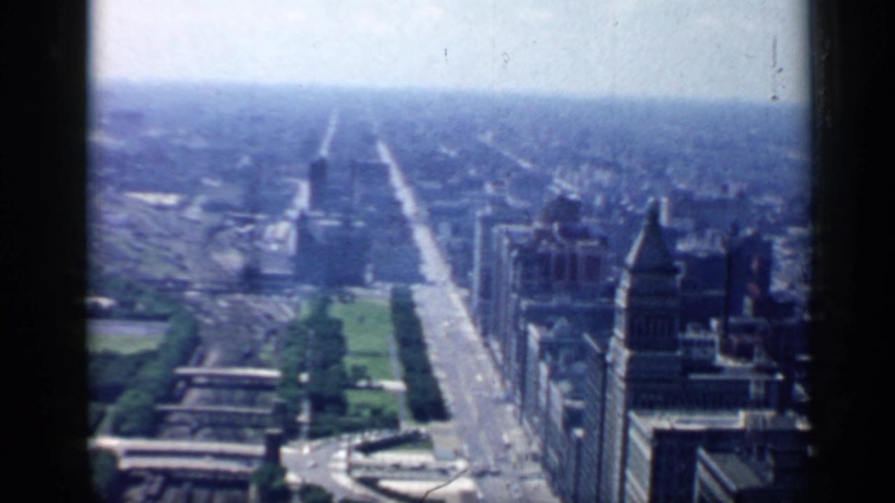 High view over a broad city avenue with towers, park strips, and a hazy skyline.