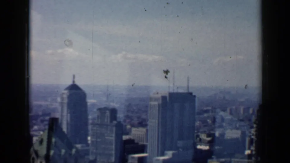 1958 8mm view of a Chicago skyline from a high window, with tall buildings softened by haze and film grain.