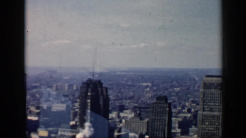 Wide 1958 Chicago skyline view with clustered high-rises, a bright hazy sky, and visible home-movie film texture.
