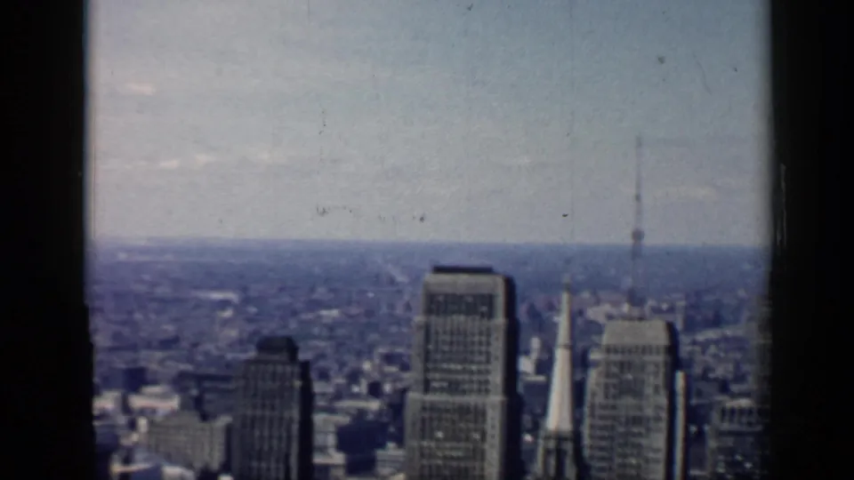 Chicago panorama on 8mm film, with high-rise buildings, a distant steeple, haze, and visible gate edges.