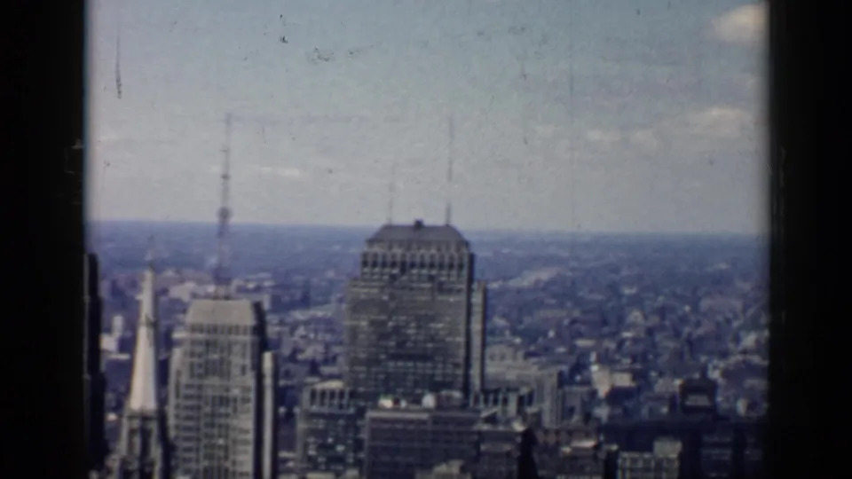 Chicago skyline near the end of the pan, with a large high-rise, clustered rooftops, distant urban blocks, and faded 8mm color.