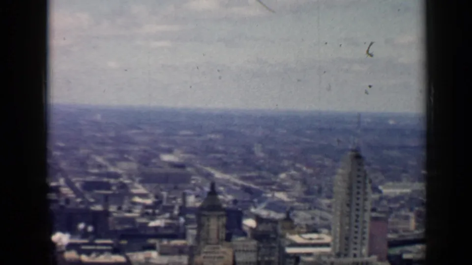 1958 Chicago panorama with a tall high-rise at right, lower rooftops and roads below, and a hazy metropolitan horizon.