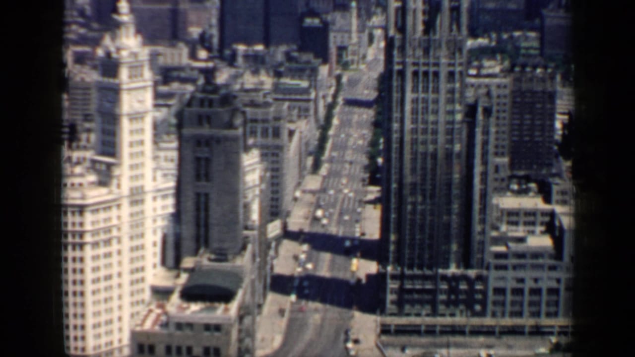 Downtown street canyon with tall buildings and a pale tower topped by a bright spire.