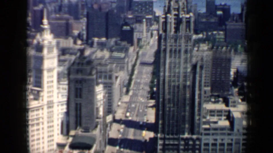 1958 8mm elevated view down a Chicago street corridor, with the pale spired tower at left and tall downtown buildings lining the roadway.